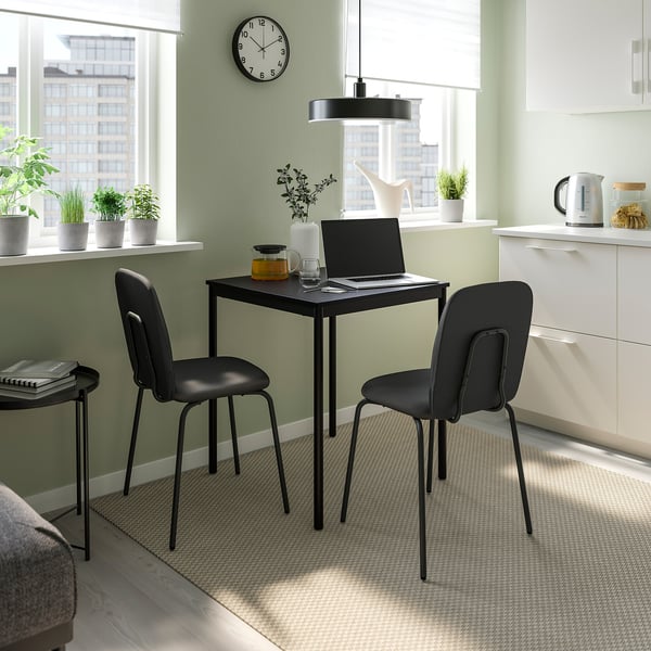 Modern workspace with black PÅBODA chair and table, laptop, plants, and kettle.