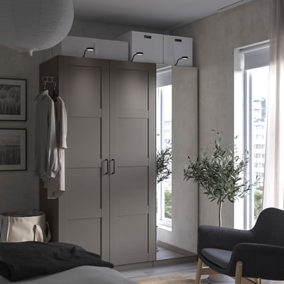 Modern bedroom gray PAX wardrobe with mirror doors, open wardrobe, hanging clothes, gray armchair, side table, window, and houseplant.