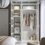 Open white PAX wardrobe displaying neatly folded clothes, hanging garments, gray storage boxes, and a laundry bag on shelves and hanging rod.
