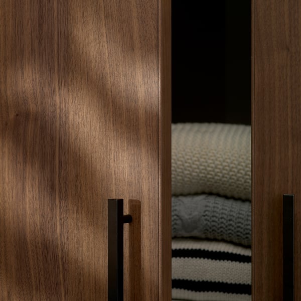 Dark wood wardrobe doors with sleek handles, partially open revealing neatly stacked blankets.