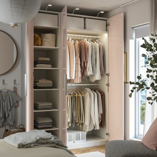 Closed PAX wardrobe displaying organized clothes, with hanging garments and shelves visible. Integrated lighting illuminates the interior.