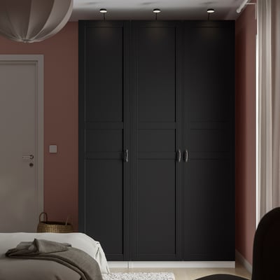 Modern bedroom with large black PAX wardrobe, next to a white door, partially covering a bed with gray blankets. Wardrobe is tall and narrow.