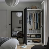 Bedroom with open wardrobe displaying clothes, folded garments, and storage boxes. Mirror on door reflects room decor.