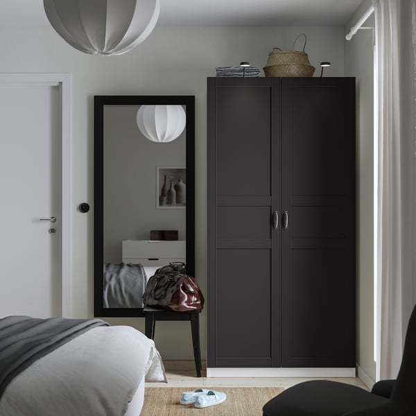 Modern bedroom with black PAX wardrobe, mirror, bed, and baskets. White pendant lights, gray rug, and sandals.