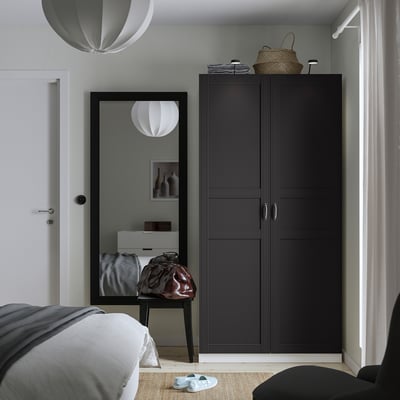Modern bedroom with black PAX wardrobe, mirror, bed, and baskets. White pendant lights, gray rug, and sandals.