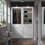 Modern white PAX wardrobe with glass doors and panel design, displaying clothes between two windows.