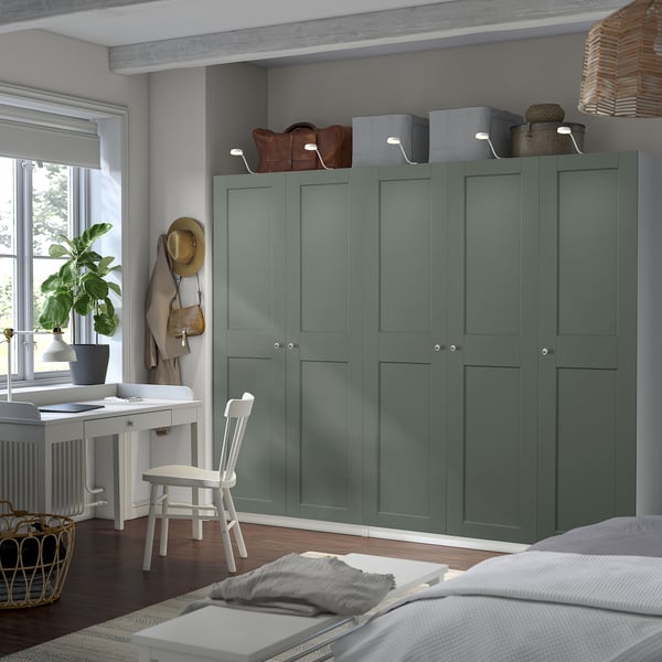 Green PAX wardrobe with multiple doors & storage. Topped with boxes & a handbag. In cozy bedroom near window with plant.