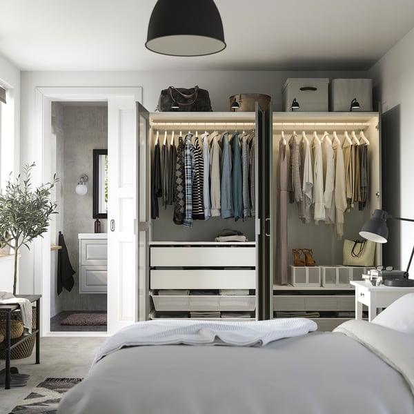 Bedroom with open wardrobe displaying clothes, bags, and organized drawers. Mirrors enhance space.
