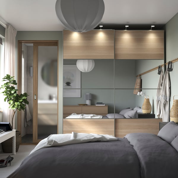 Modern grey bedroom with PAX wardrobe, wooden panels, glass doors, hanging clothes, wall hooks, and a plant.