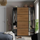 Bedroom with a PAX wardrobe, sliding mirrored doors, clothes inside, and a bed with blanket.