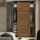 Bedroom with wooden sliding door wardrobe, hanging clothes, shelves, and drawers.