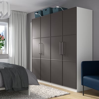 A room with a large black PAX wardrobe, sliding doors. Minimalist decor, grey bed, blue chair, pendant lamp, and large window.