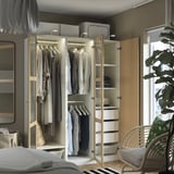 Modern bedroom with open wardrobe showcasing clothes, shelves, and drawers. Integrated lighting illuminates organized storage solutions.