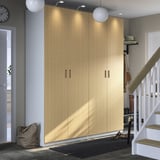 Large wooden PAX wardrobe in hallway, lit by overhead lights. Next to stairs and entry door, with a black mat and a bag.
