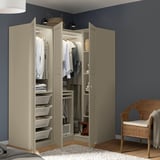 A modern beige wardrobe with open doors reveals neatly organized clothes, shelves, and white laundry baskets. It stands against a dark blue wall.