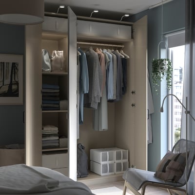 Modern closet with gray PAX wardrobe, hanging clothes, shelves, and storage bins. Natural light from window.