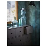 Green room with black dresser, blue head sculpture, vases, and lamp.