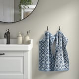 Blue PILGULDMAL towels hang near white sink, round mirror above, beige dispensers with toothbrushes.