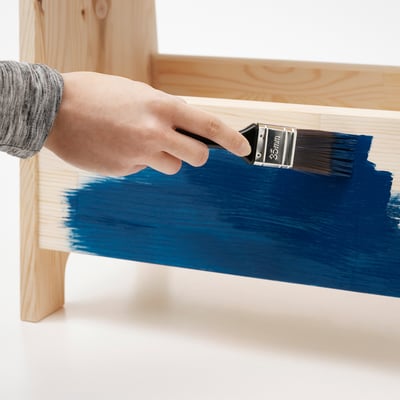 Person painting a wooden chair with blue colour, using 35mm brush.