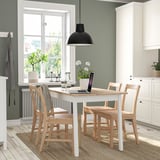 Cozy dining area with white table, wooden chairs, plants, and candles.