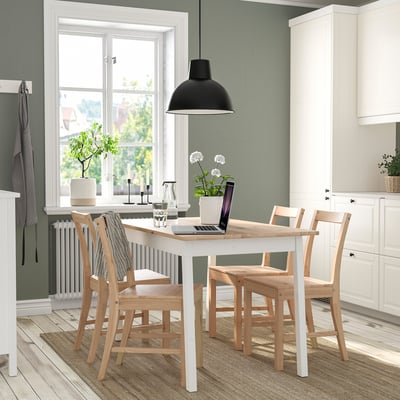 Cozy dining area with white table, wooden chairs, plants, and candles.