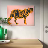 PJÄTTERYD orange tiger print with pink background, framed, above wooden surface with green vase and plant.