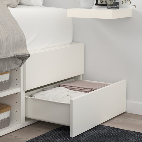 Bed with open storage drawer under white lid, showing folded blankets.