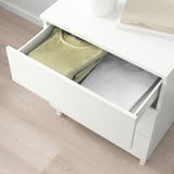 White PLATSA chest with open drawer revealing folded clothes. Easy-to-assemble storage with adjustable feet for uneven floors.