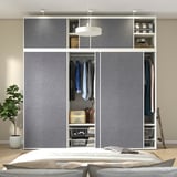 Bedroom closet with sliding doors, hanging clothes, shelves, and light fixture. Plant on left, bed in foreground.