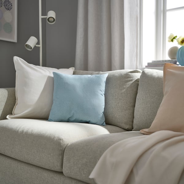 Modern living room with gray sofa, light blue PROFETBLOMMA cushion, white pillows, light-colored throw, and decorative items.