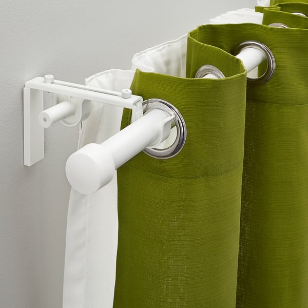 A white dual curtain rod system with green and white curtains hanging, demonstrating its flexibility for layered curtains.