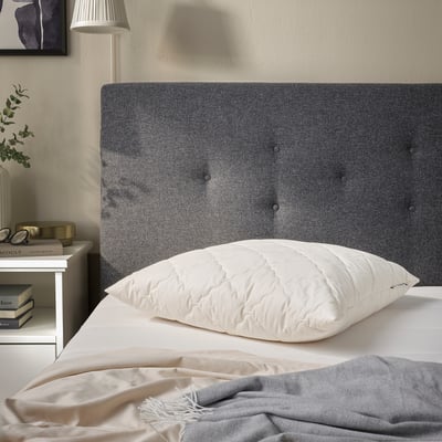 Grey RÅDHUSVIN pillow on bed, larger than books, with white quilt, silk cover, modern decor.