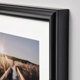 Black-framed artwork hangs on a light-colored wall. The frame has a sleek, polished finish showing high-quality craftsmanship.