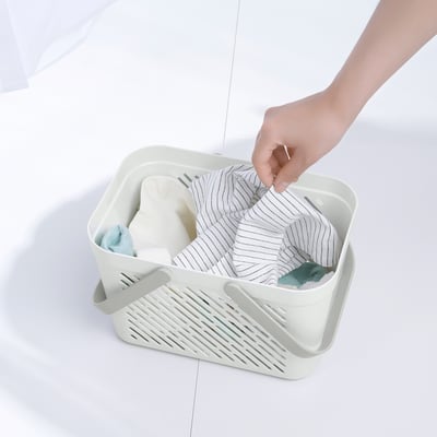 Hand places item into white RÅNEN storage basket filled with towels and toiletries, showcasing its practical use for organizing bathroom essentials.