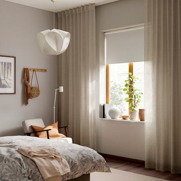 Minimalist bedroom with beige curtains, pendant light, bed, chair, plant, and decor.