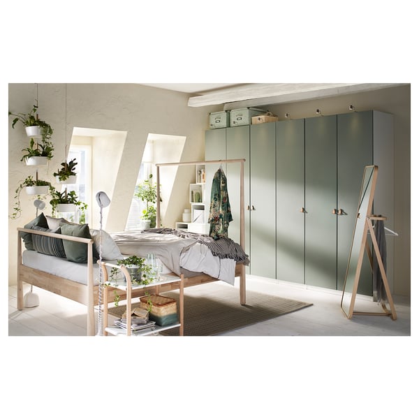 Modern bedroom with light wood bed, green closets, and numerous hanging plants.
