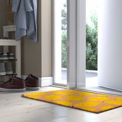Bright yellow RENKAVLE doormat with lemon design, smaller than nearby dark brown shoes, fits under entrance hooks and next to shoe shelves.