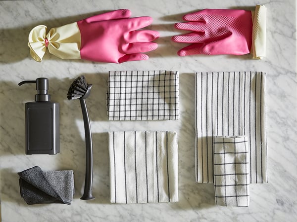 Image shows cleaning supplies: pink gloves, soap dispenser, brush, cloths, and towels on marble.