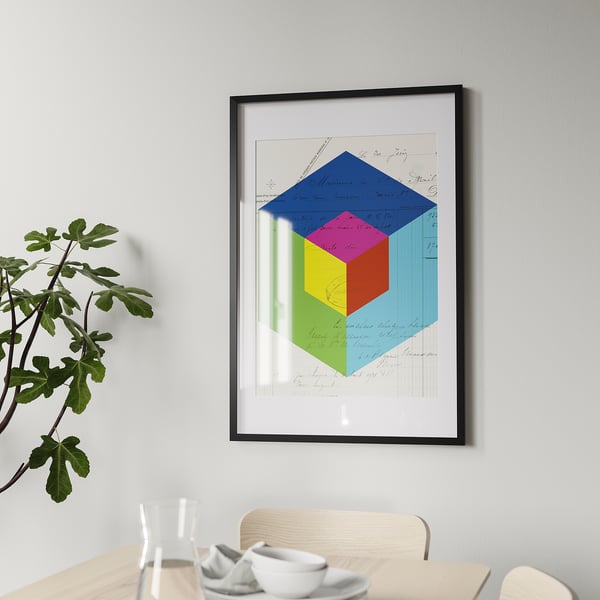 Geometric poster in black frame on gray wall, with dining table and plant.