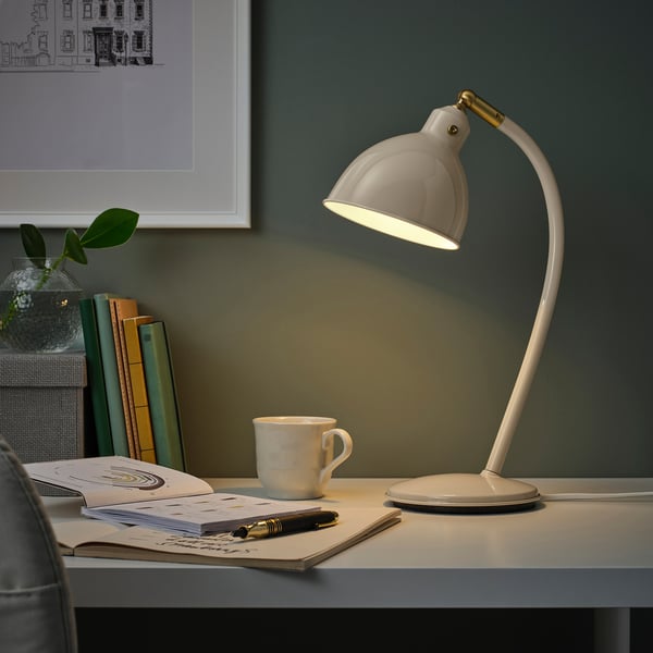 White brass desk lamp lit, illuminating cluttered workspace.