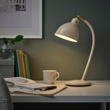 White brass desk lamp lit, illuminating cluttered workspace.