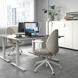 Modern sit-stand desk in office with two monitors, laptop, ergonomic chairs, and city view.