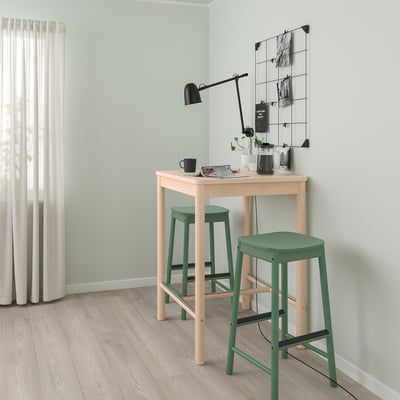 Minimalist green RÖNNINGE bar stool with open back, footrest, under table. Black lamp, white curtains.