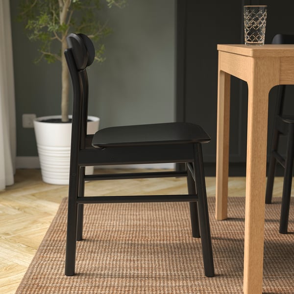 Black wooden chair with visible grain, soft rounded seat and back, placed near a wooden table.