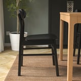 Black wooden chair with visible grain, soft rounded seat and back, placed near a wooden table.
