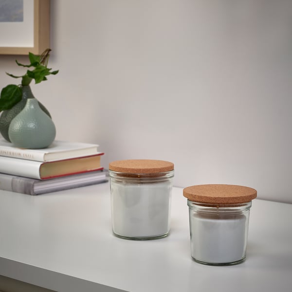 Two glass jars with cork lids on a white table, one holding a white candle.