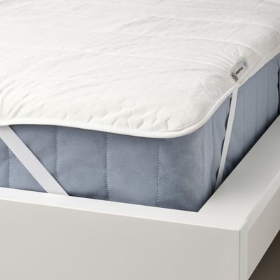 A white mattress protector with elastic corners, featuring a cooling fabric and temperature-regulating wax fibers, displayed on a bed frame.