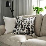 Beige couch with herbarium-inspired throw pillow and floor lamp.