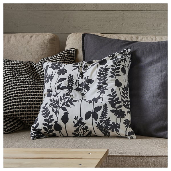 A square throw pillow on a couch. The pillow is white with black floral designs and has a zipper.