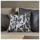 A square throw pillow on a couch. The pillow is white with black floral designs and has a zipper.